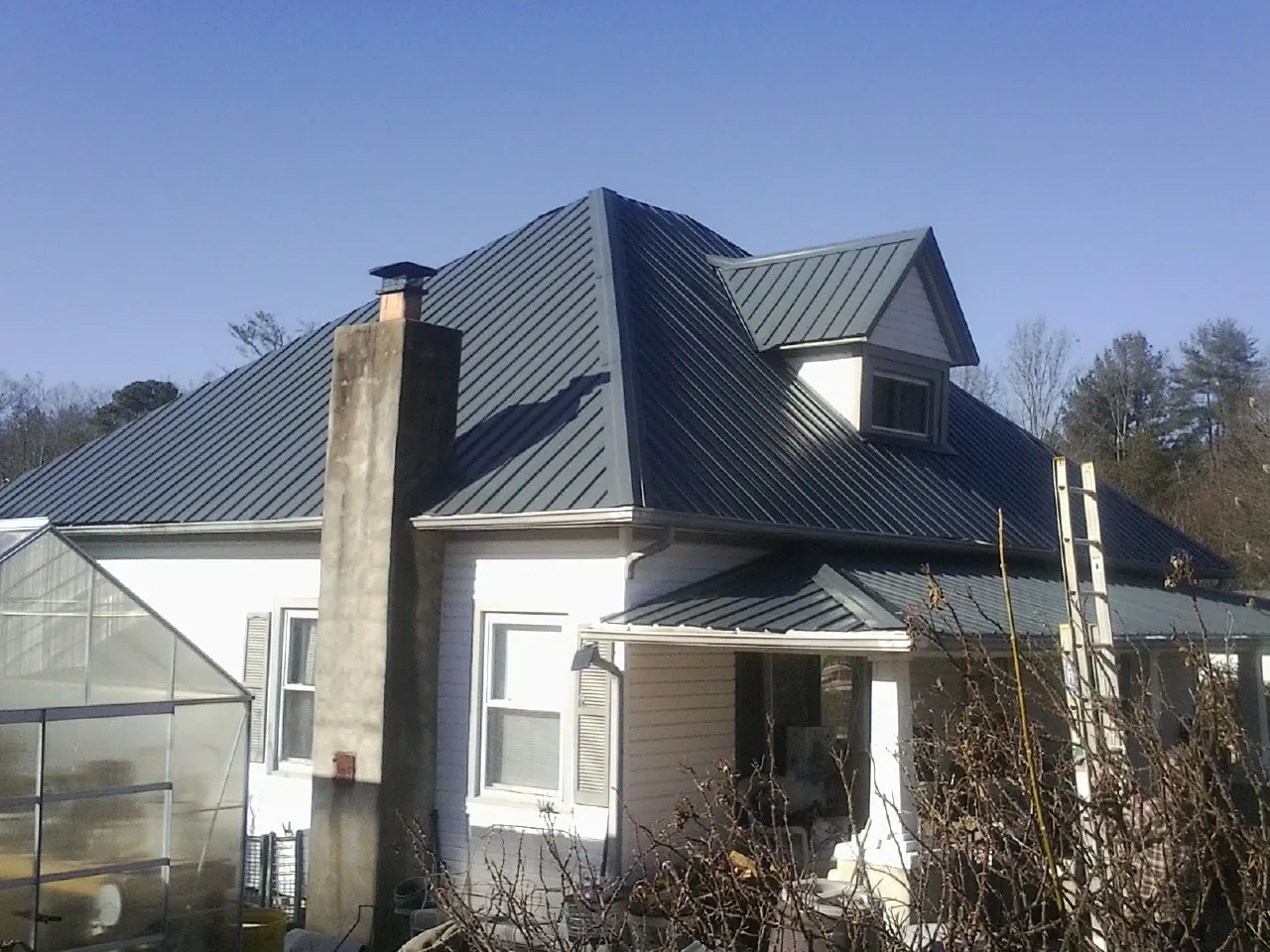 Dark blue standing seam metal roof on a white farmhouse with dormer — Slate & Tile Roof Repair by Roofing Brothers in Short Hills