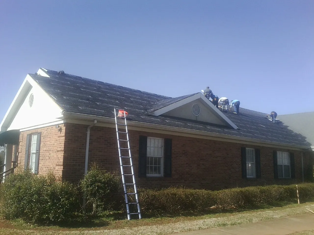 Crew tearing shingles off a brick ranch roof with a ladder set — Emergency Roof Repair work by our crew in Short Hills