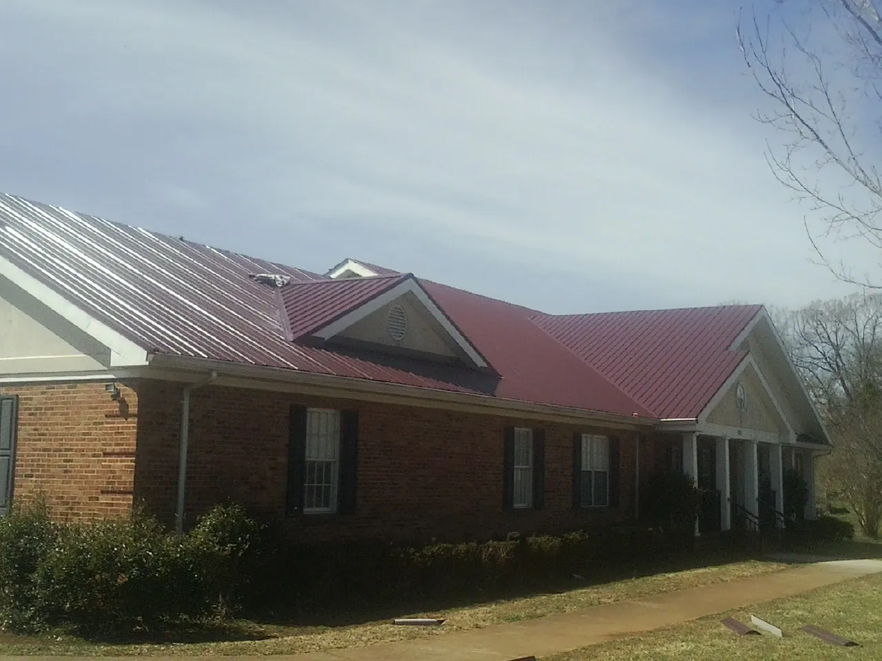 Red metal roof with gabled entries on a long brick building, from a Hail Damage Roof Repair job in Short Hills