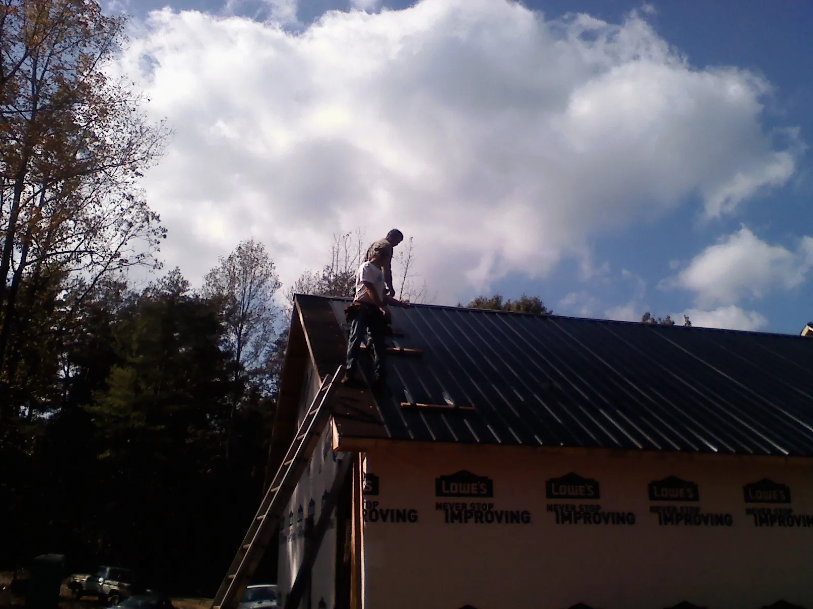 Roofer fastening dark metal panels high against a cloudy sky, from a Roof Inspection job in Short Hills