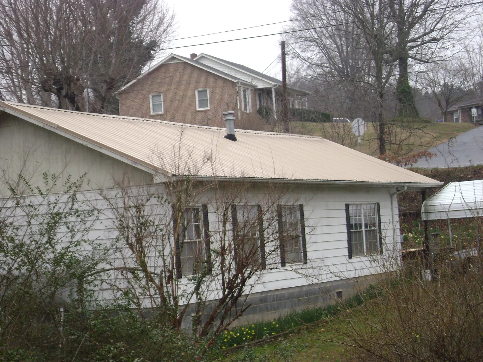 Tan metal roof on a white sided house set into a hillside — Commercial Roofing by Roofing Brothers in Short Hills